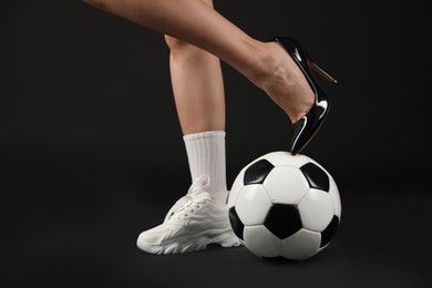 Photo of Woman in high heeled shoe and sneaker with soccer ball on dark background, closeup