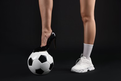 Photo of Woman in high heeled shoe and sneaker with soccer ball on dark background, closeup