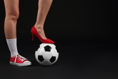 Photo of Woman in high heeled shoe and sneaker with soccer ball on dark background, closeup. Space for text