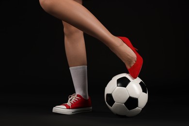 Photo of Woman in high heeled shoe and sneaker with soccer ball on dark background, closeup