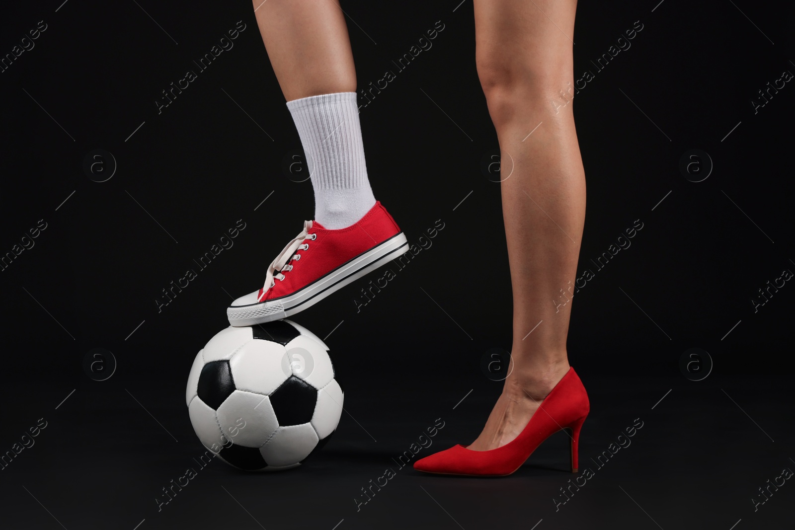 Photo of Woman in high heeled shoe and sneaker with soccer ball on dark background, closeup