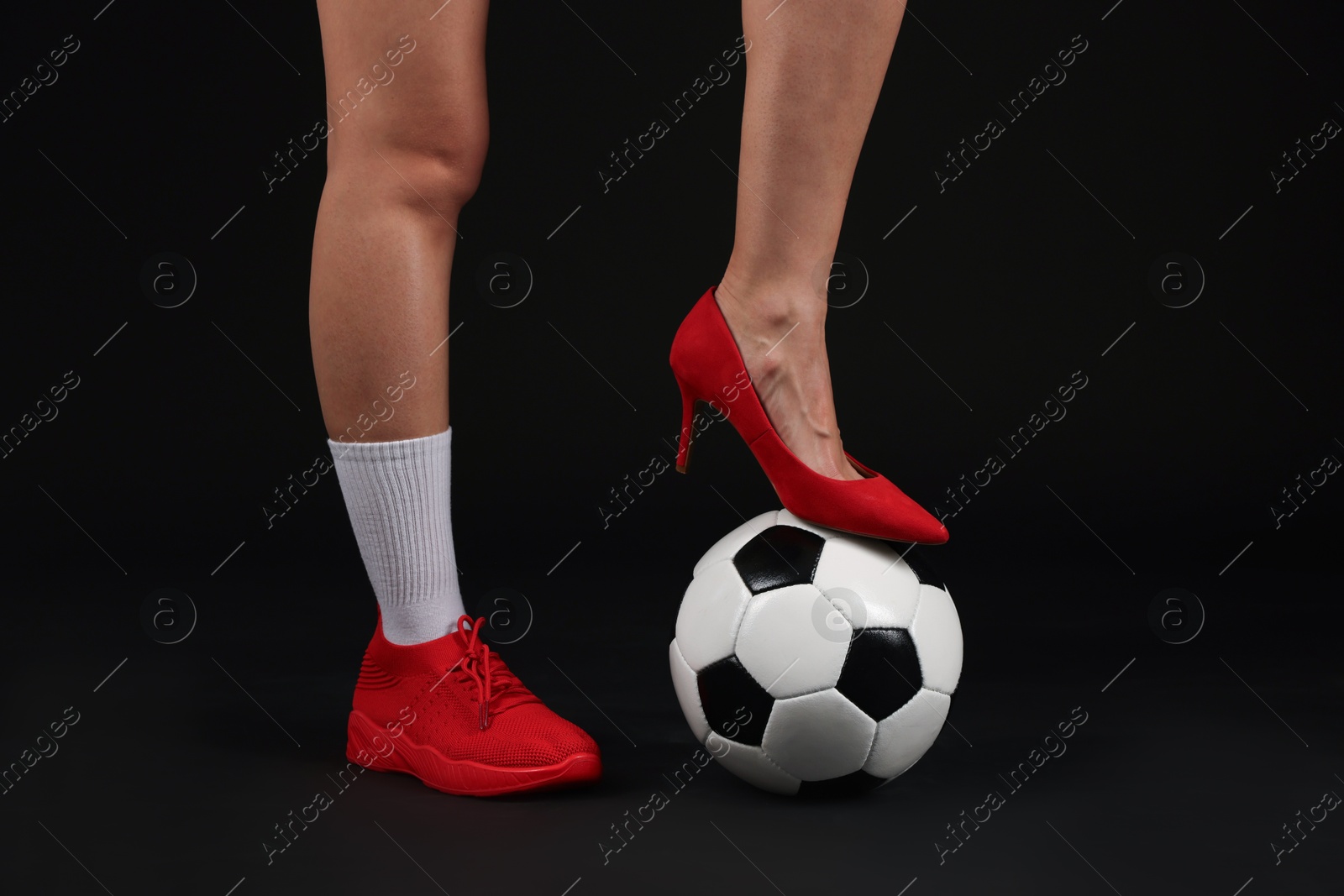 Photo of Woman in high heeled shoe and sneaker with soccer ball on dark background, closeup