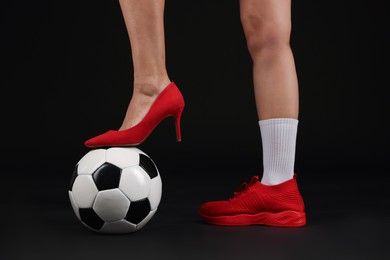 Photo of Woman in high heeled shoe and sneaker with soccer ball on dark background, closeup