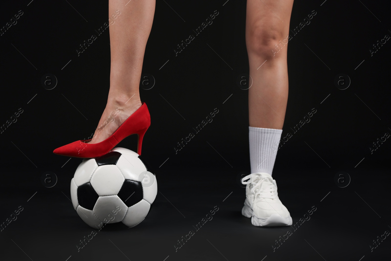 Photo of Woman in high heeled shoe and sneaker with soccer ball on dark background, closeup