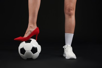 Photo of Woman in high heeled shoe and sneaker with soccer ball on dark background, closeup