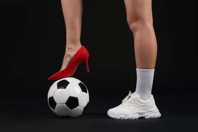 Photo of Woman in high heeled shoe and sneaker with soccer ball on dark background, closeup