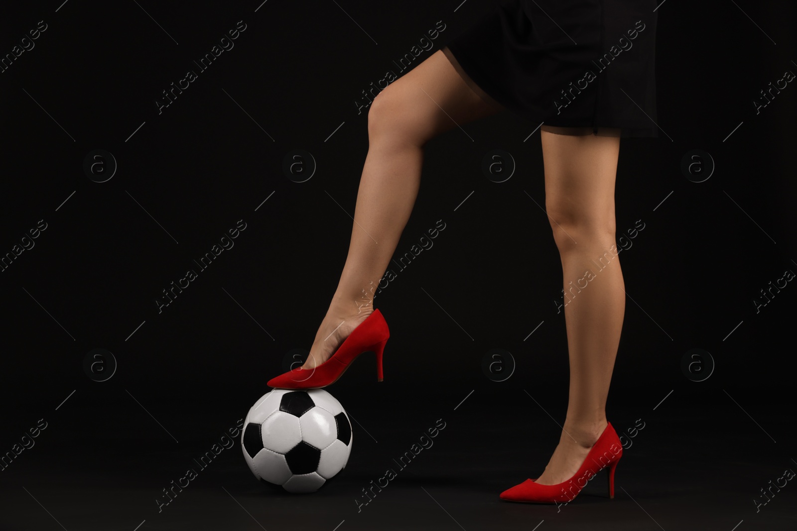 Photo of Woman in high heeled shoes with soccer ball on dark background, closeup
