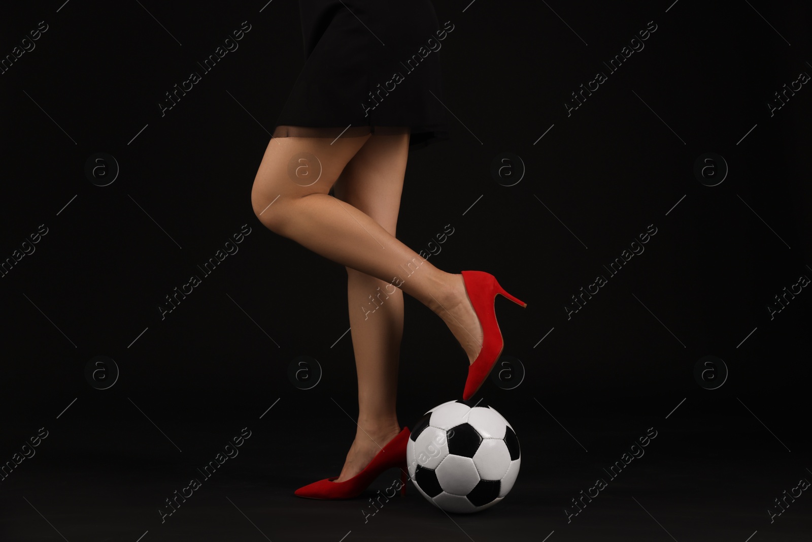 Photo of Woman in high heeled shoes with soccer ball on dark background, closeup