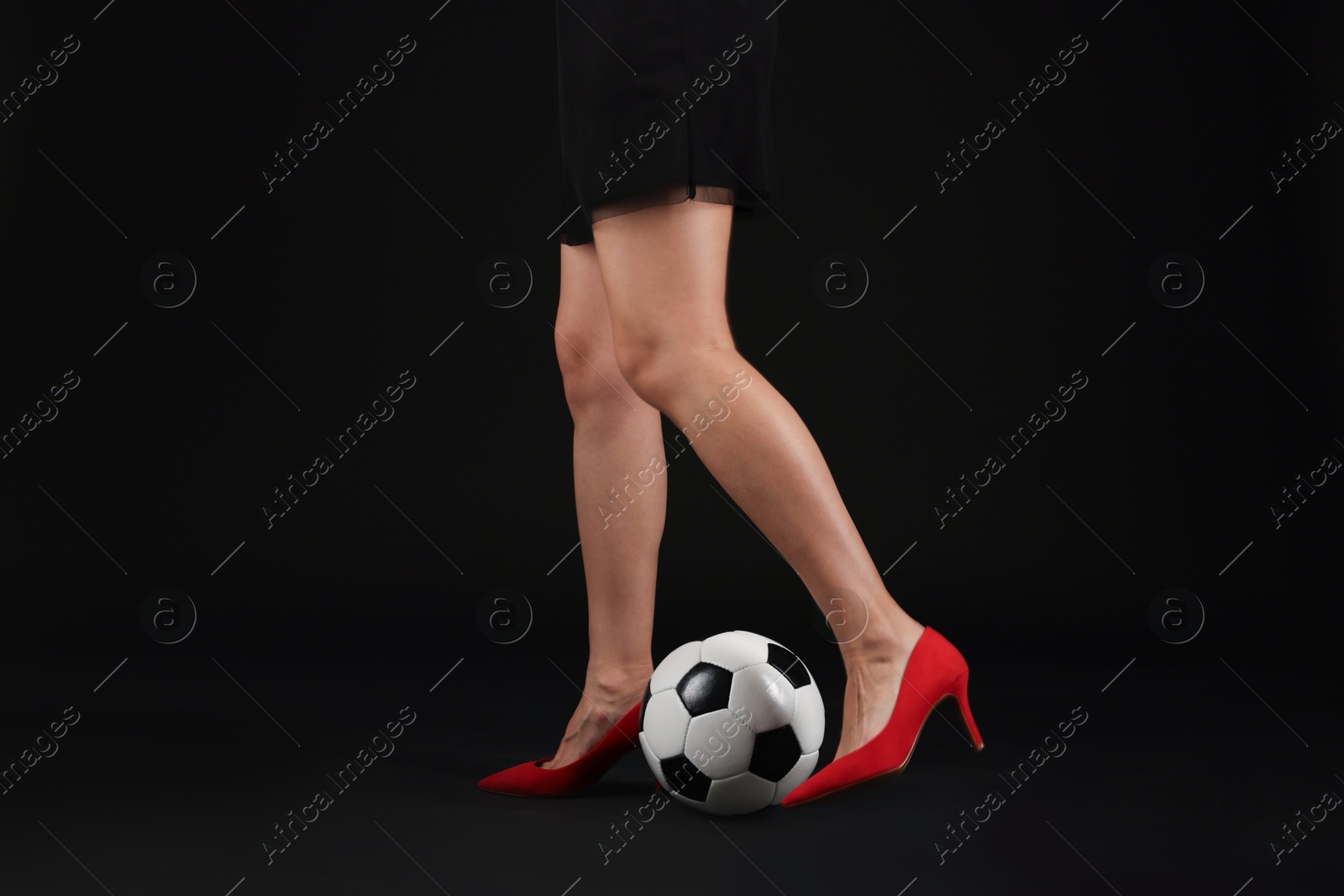 Photo of Woman in high heeled shoes with soccer ball on dark background, closeup