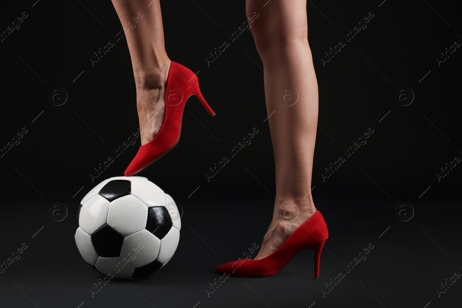 Photo of Woman in high heeled shoes with soccer ball on dark background, closeup