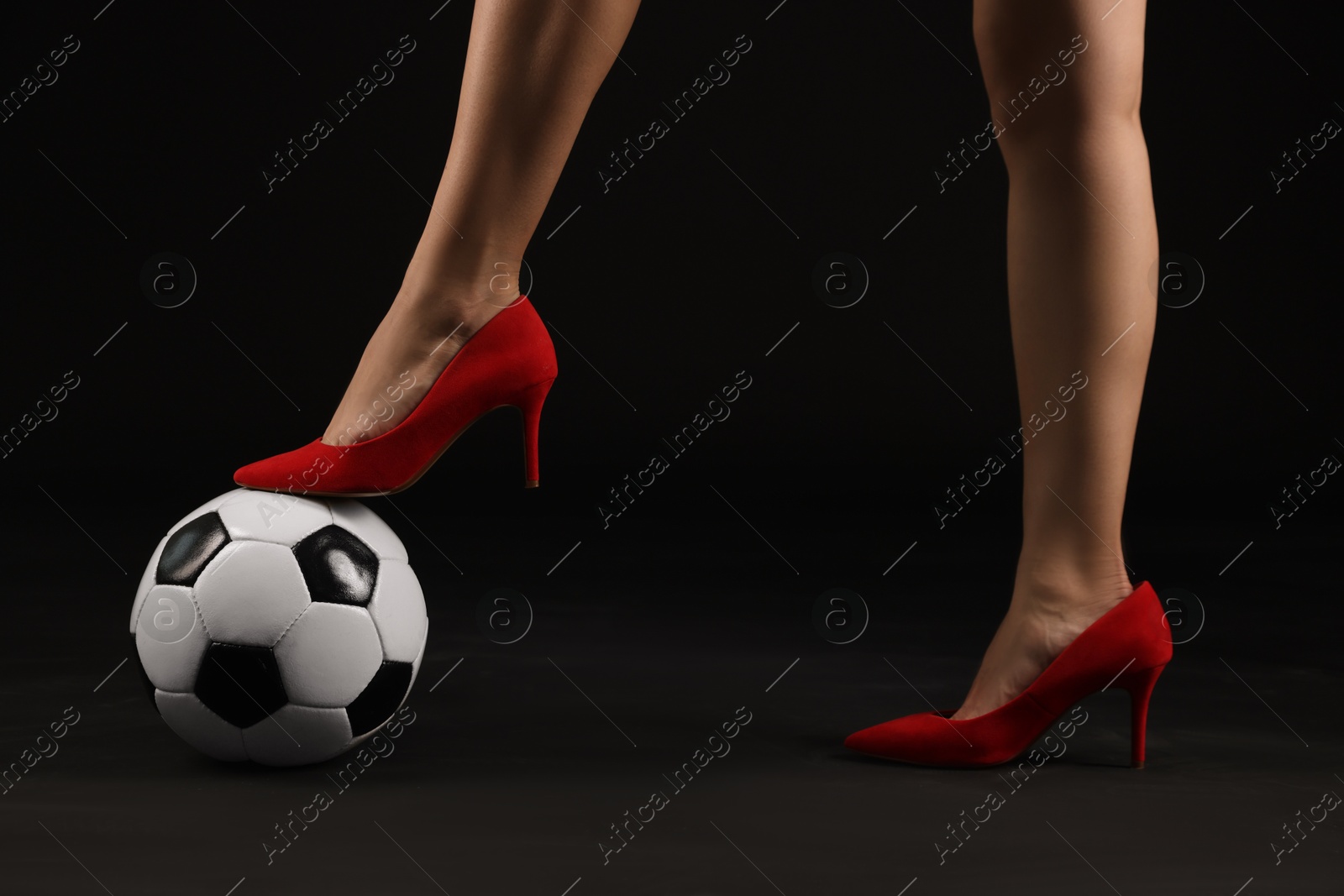 Photo of Woman in high heeled shoes with soccer ball on dark background, closeup