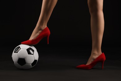Photo of Woman in high heeled shoes with soccer ball on dark background, closeup