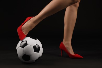 Photo of Woman in high heeled shoes with soccer ball on dark background, closeup