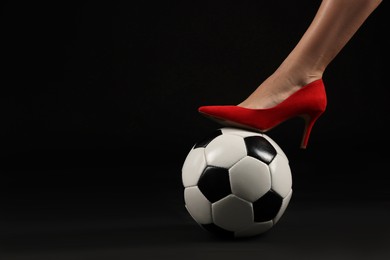 Photo of Woman in high heeled shoe with soccer ball on dark background, closeup. Space for text