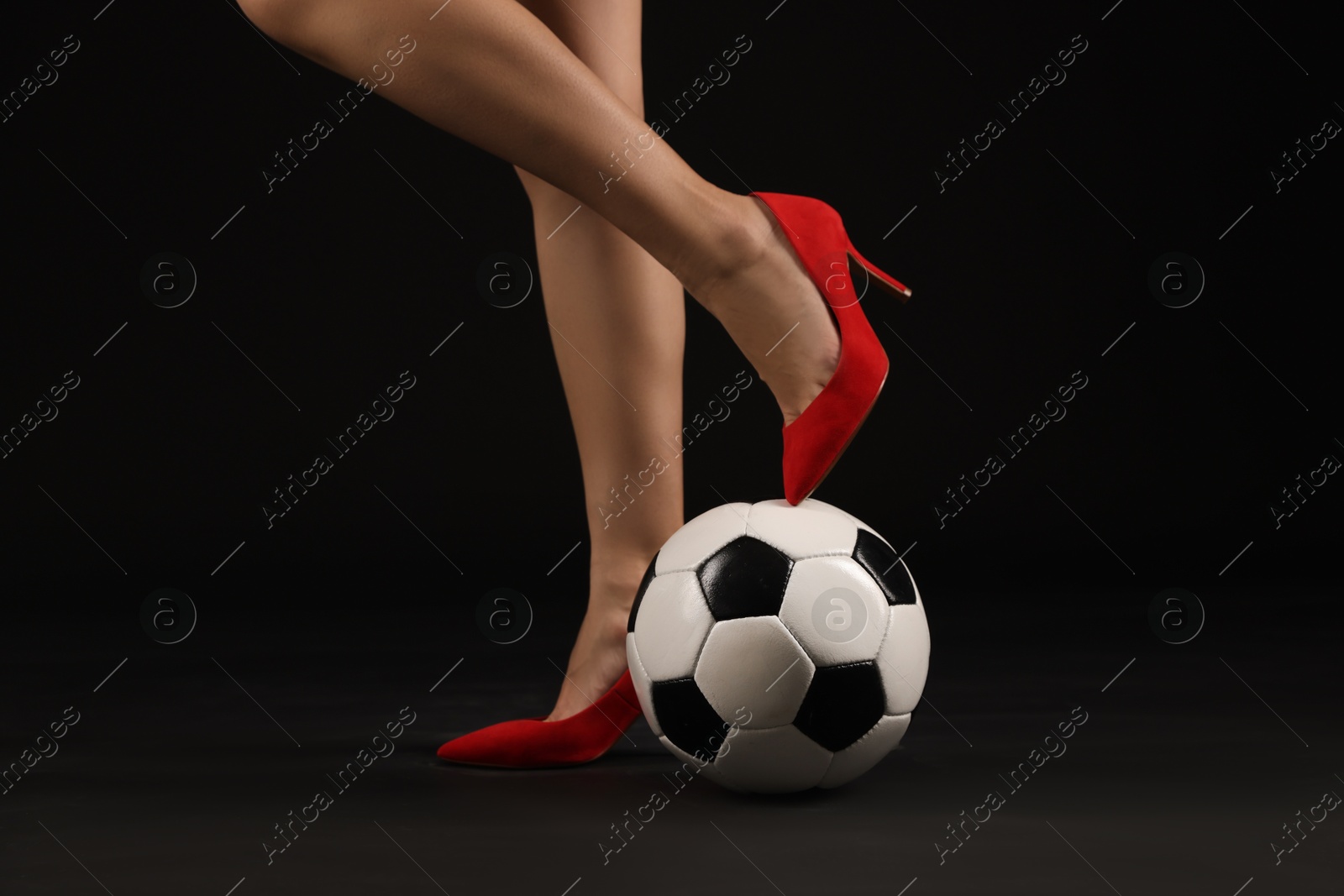 Photo of Woman in high heeled shoes with soccer ball on dark background, closeup