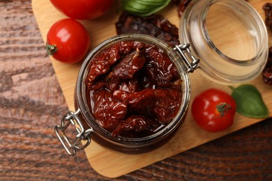 Photo of Tasty sun dried tomatoes and fresh vegetables on wooden table, top view