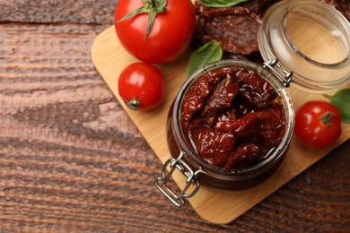 Photo of Tasty sun dried tomatoes and fresh vegetables on wooden table, top view. Space for text