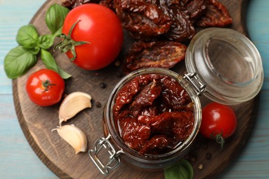 Photo of Tasty sun dried tomatoes, fresh vegetables and peppercorns on light blue wooden table, top view