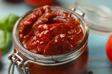 Photo of Tasty sun dried tomatoes in jar on light blue table, closeup