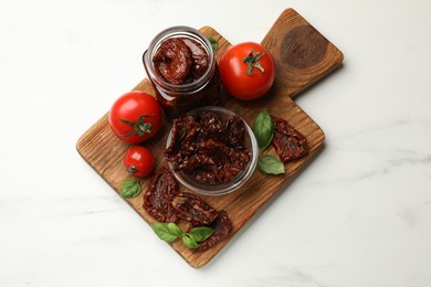 Photo of Tasty sun dried tomatoes and fresh vegetables on white marble table, top view