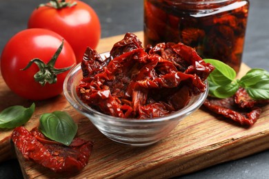 Photo of Tasty sun dried tomatoes and fresh vegetables on black table, closeup