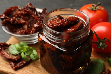 Photo of Tasty sun dried tomatoes and fresh vegetables on black table, closeup