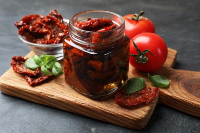 Photo of Tasty sun dried tomatoes and fresh vegetables on black table, closeup