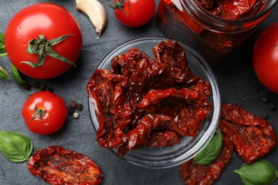 Photo of Tasty sun dried tomatoes, fresh vegetables and peppercorns on black table, flat lay