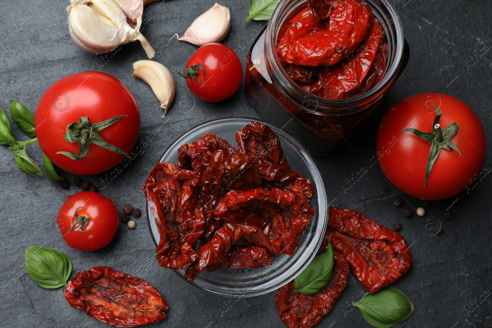 Tasty sun dried tomatoes, fresh vegetables and peppercorns on black table, flat lay Photo of Tasty sun dried tomatoes, fresh vegetables and peppercorns on black table, flat lay