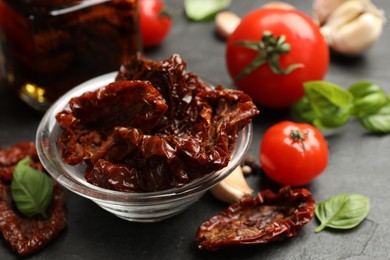 Photo of Tasty sun dried tomatoes and fresh vegetables on black table, closeup