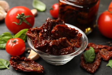 Photo of Tasty sun dried tomatoes and fresh vegetables on black table, closeup