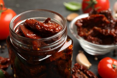 Photo of Tasty sun dried tomatoes and fresh vegetables on black table, closeup