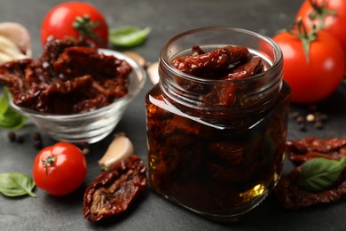 Photo of Tasty sun dried tomatoes and fresh vegetables on black table, closeup