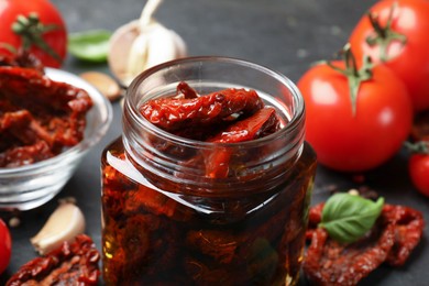 Photo of Tasty sun dried tomatoes and fresh vegetables on black table, closeup