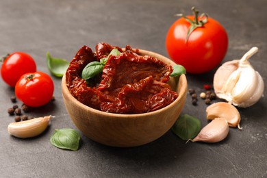 Photo of Tasty sun dried tomatoes and fresh vegetables on black table, closeup