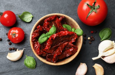 Photo of Tasty sun dried tomatoes, fresh vegetables and peppercorns on black table, flat lay