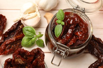 Photo of Tasty sun dried tomatoes and fresh vegetables on light wooden table, top view