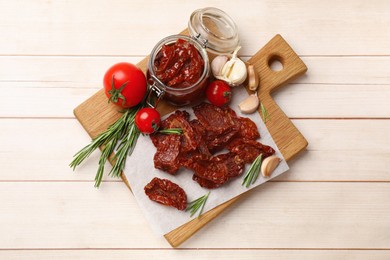 Photo of Tasty sun dried tomatoes and fresh vegetables on light wooden table, top view