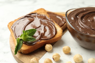 Photo of Tasty chocolate spread with mint and hazelnuts on white marble table, closeup