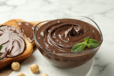 Photo of Tasty chocolate spread with mint and hazelnuts on white marble table, closeup