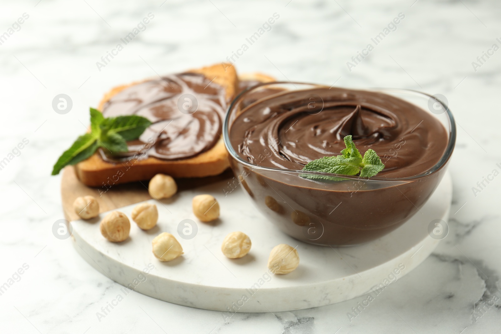 Tasty chocolate spread with mint and hazelnuts on white marble table, closeup Photo of Tasty chocolate spread with mint and hazelnuts on white marble table, closeup