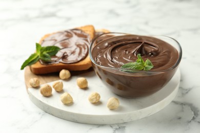 Photo of Tasty chocolate spread with mint and hazelnuts on white marble table, closeup