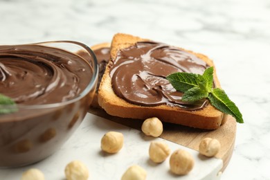 Photo of Tasty chocolate spread with mint and hazelnuts on white marble table, closeup