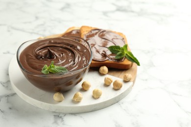 Photo of Tasty chocolate spread with mint and hazelnuts on white marble table, closeup