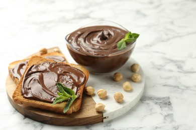 Photo of Tasty chocolate spread with mint and hazelnuts on white marble table, closeup