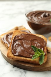 Photo of Tasty chocolate spread with mint and hazelnuts on white marble table, closeup