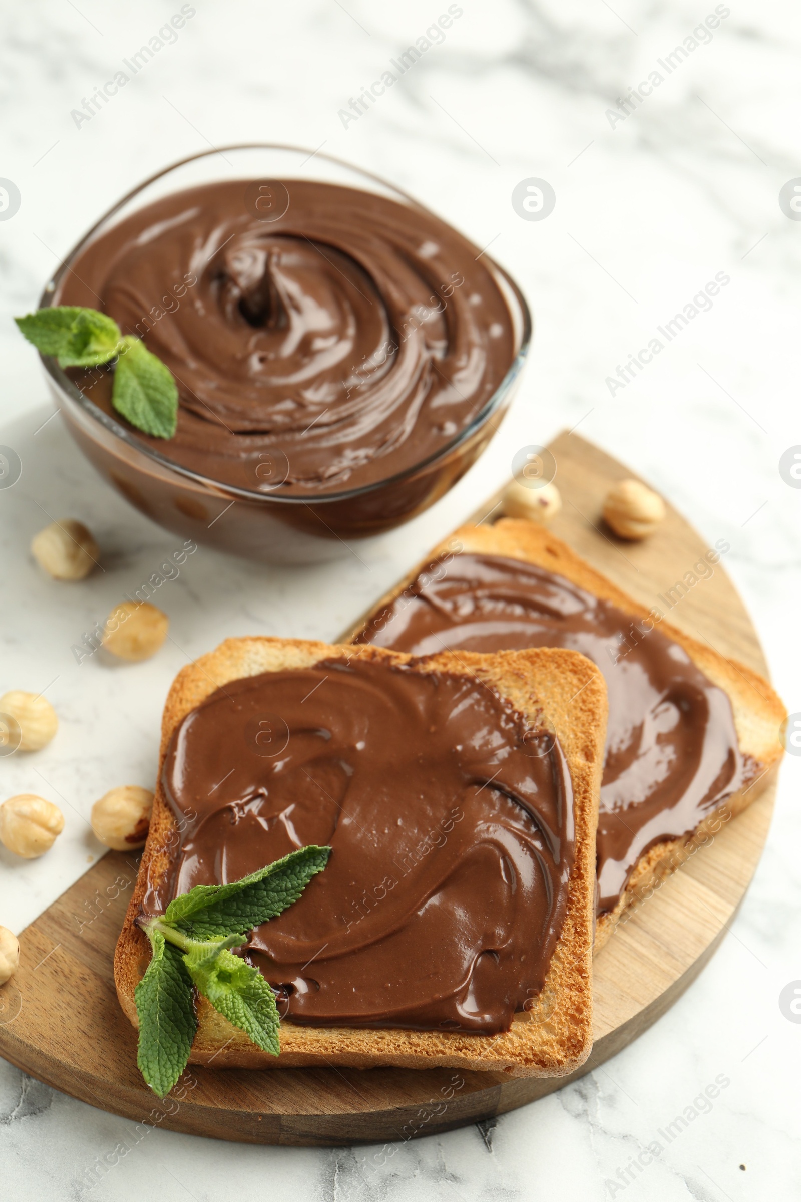 Tasty chocolate spread with mint and hazelnuts on white marble table, closeup Photo of Tasty chocolate spread with mint and hazelnuts on white marble table, closeup
