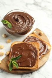 Photo of Tasty chocolate spread with mint and hazelnuts on white marble table, closeup