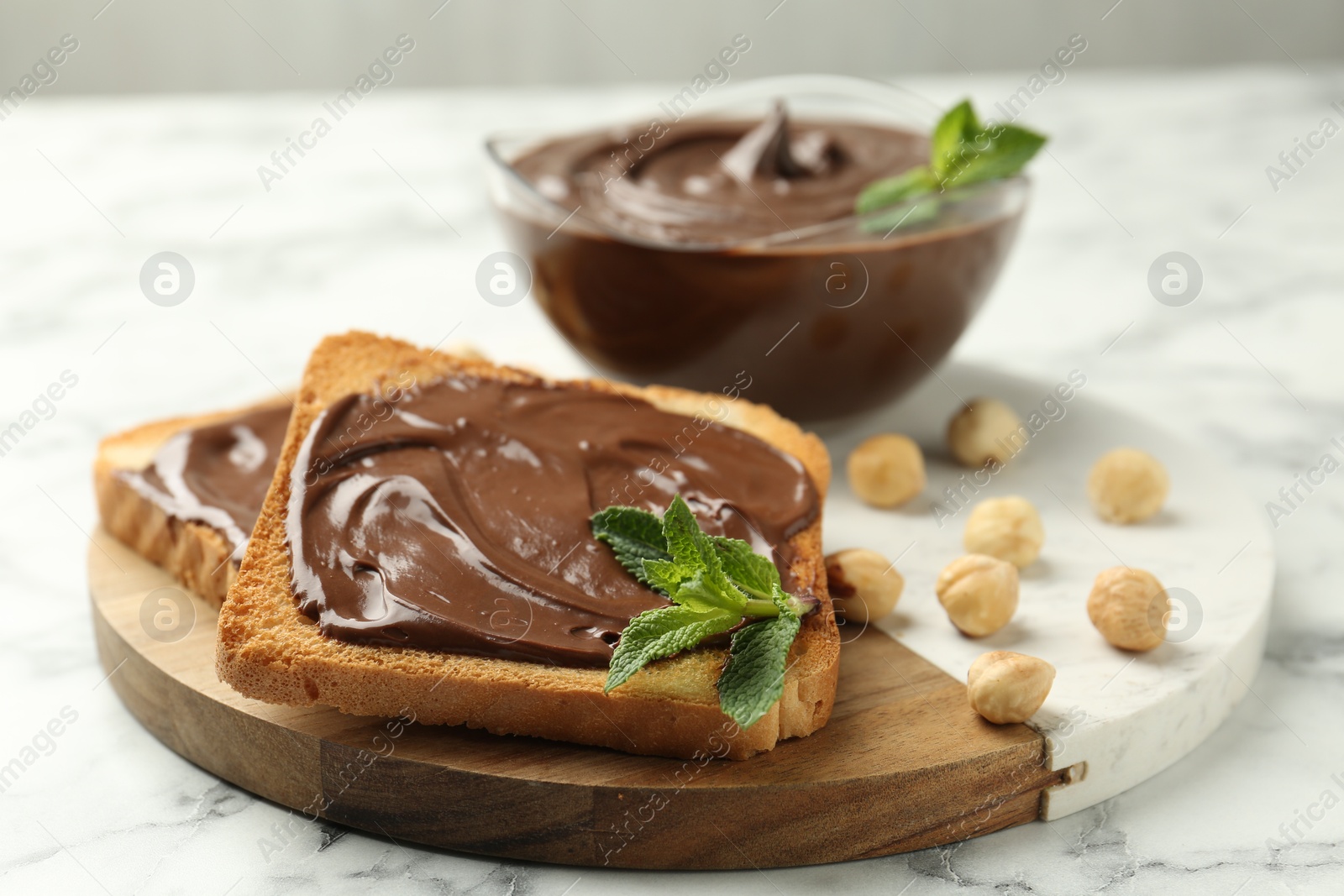 Tasty chocolate spread with mint and hazelnuts on white marble table, closeup Photo of Tasty chocolate spread with mint and hazelnuts on white marble table, closeup
