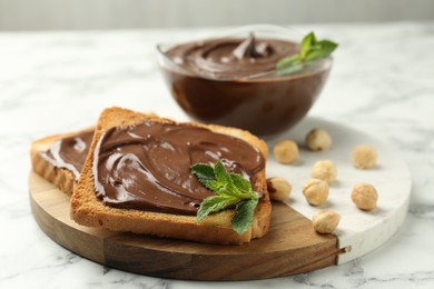 Photo of Tasty chocolate spread with mint and hazelnuts on white marble table, closeup